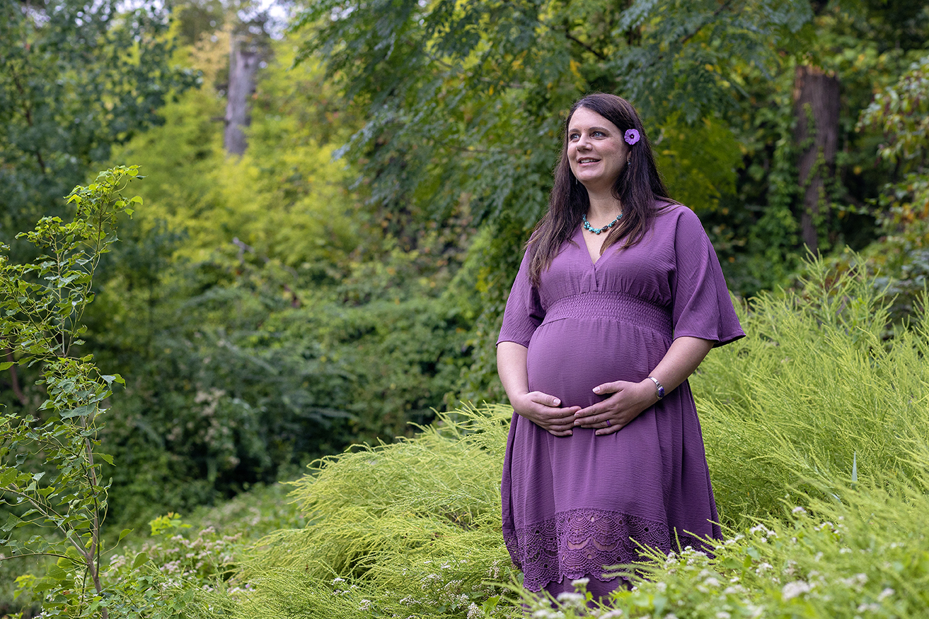 pregnant woman taking maternity photos in a long purple dress in a green grassy field