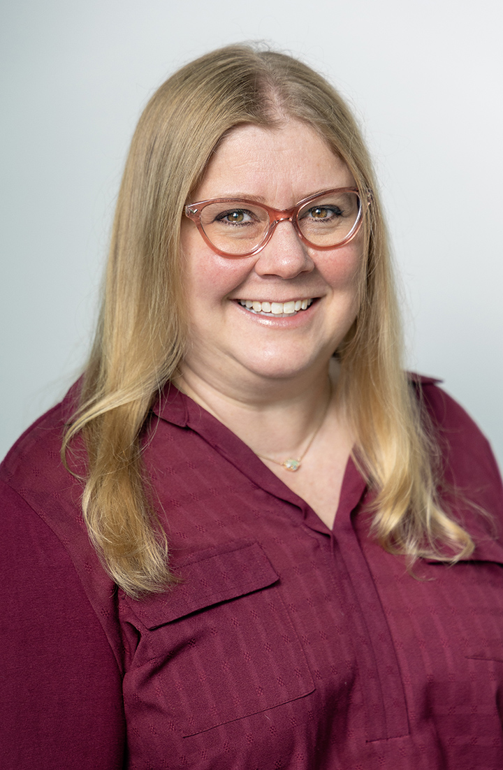 headshot portrait of a blonde woman in glasses wearing a purple shirt