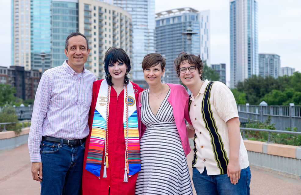 graduating senior in her red cap and gown with her family on the pedestrian bridge in downtown austin, texas