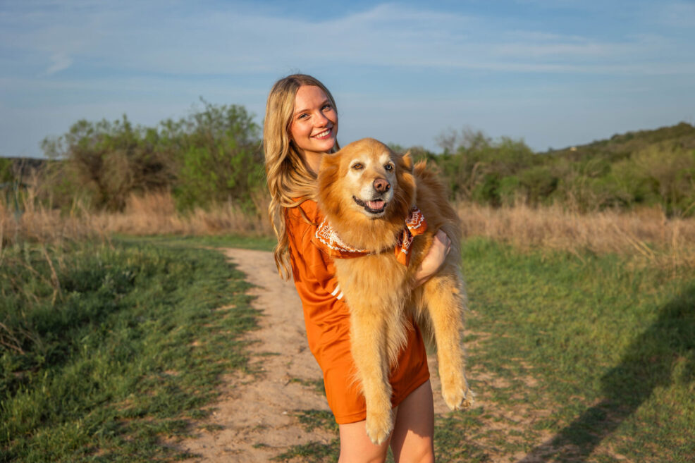 high school senior holding her pet golden retriever dog at commons ford ranch for photo session in austin