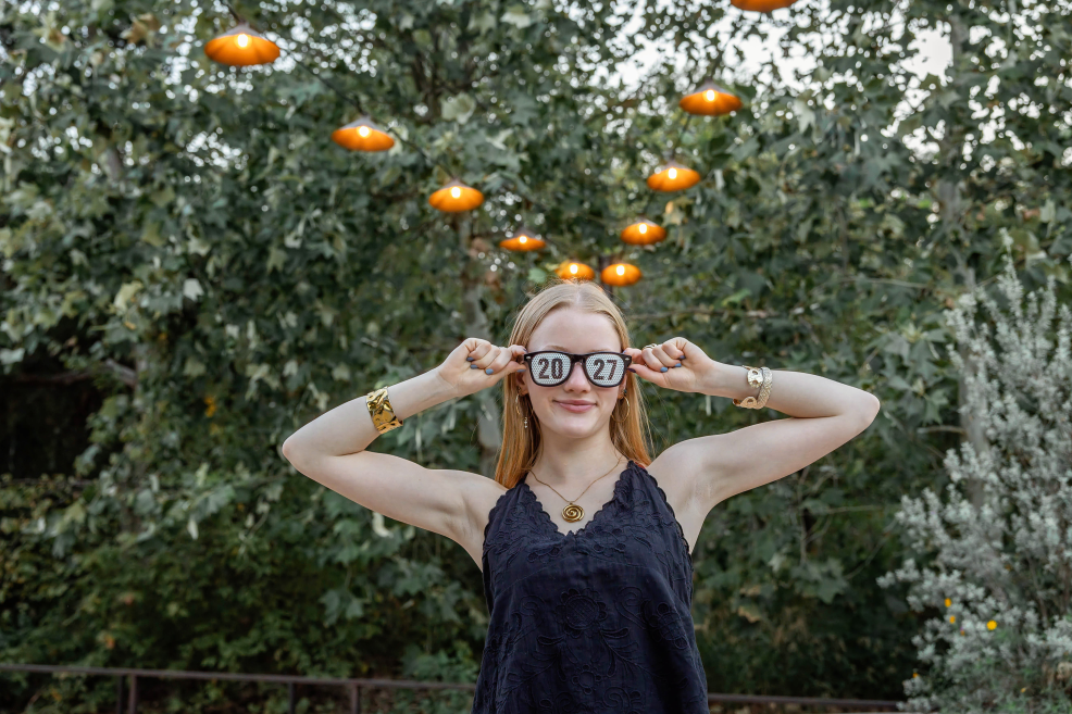 high school senior photo session at kingbury commons under the string lights with class of 2027 sunglasses on